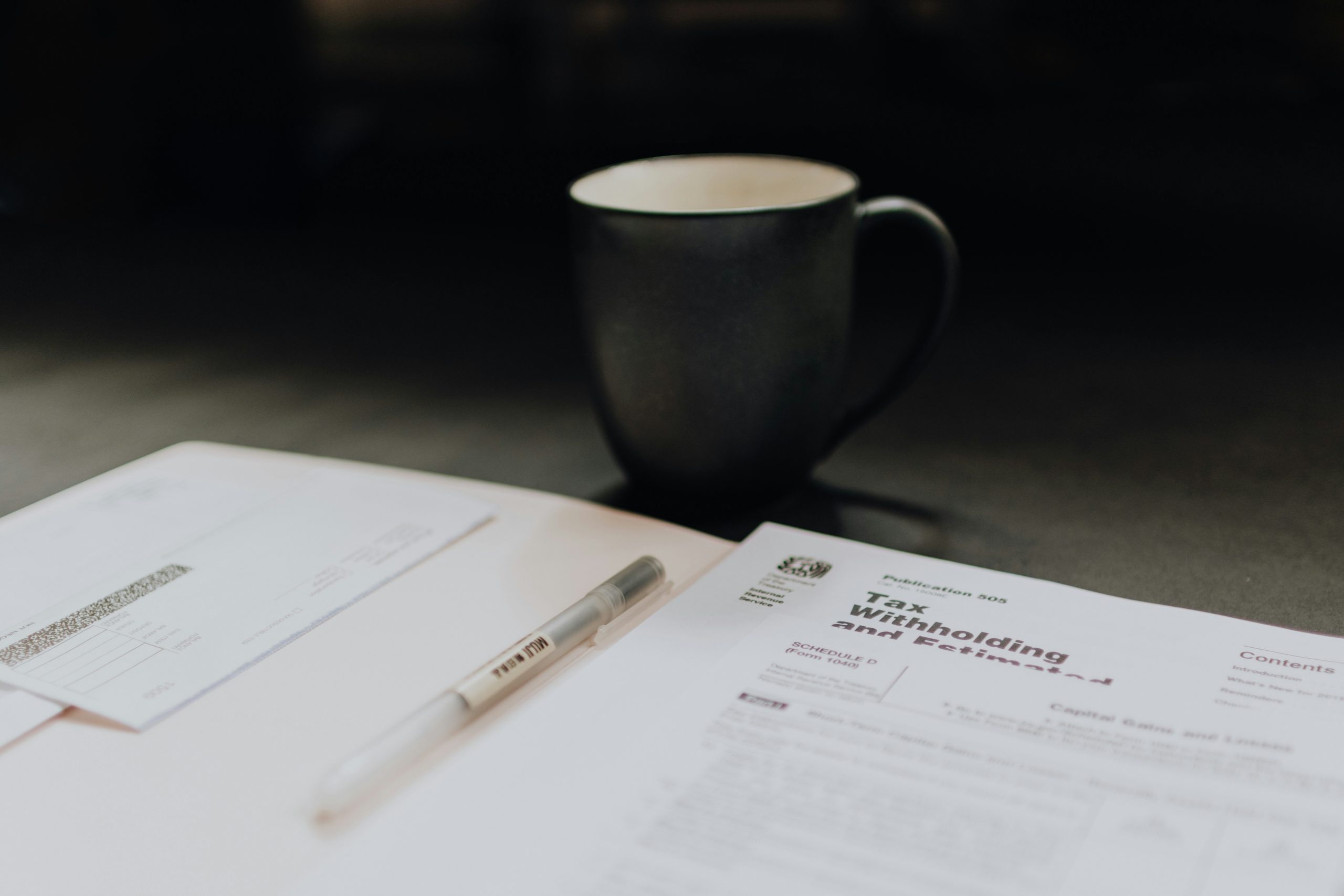 IRS tax withholding and estimated tax publication next to a pen and coffee mug on a desk