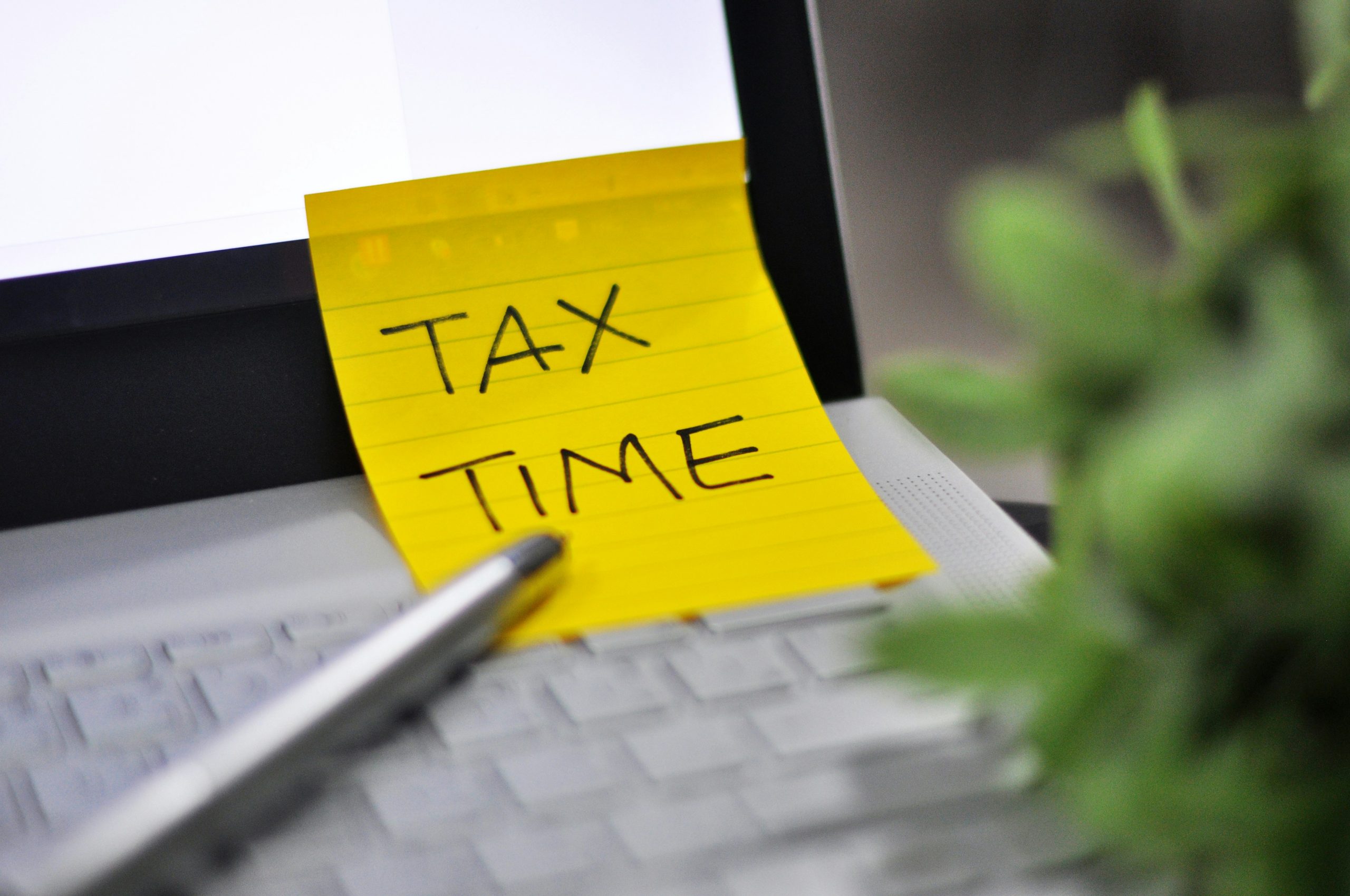 A sticky note reading tax time on a laptop keyboard as a reminder to file a first tax return