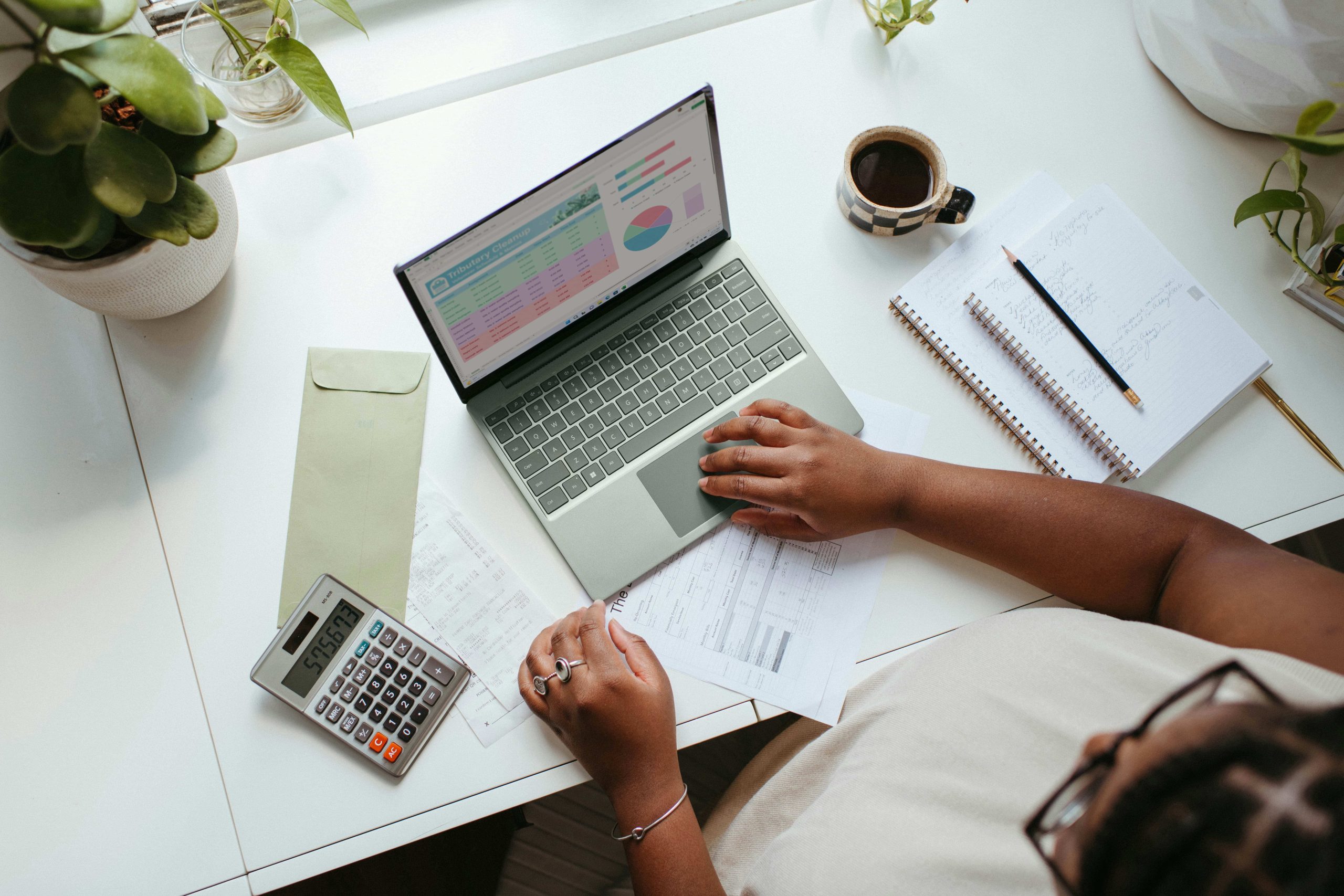 A small business owner reviewing worker classification documents on a laptop with a calculator and tax paperwork on a desk